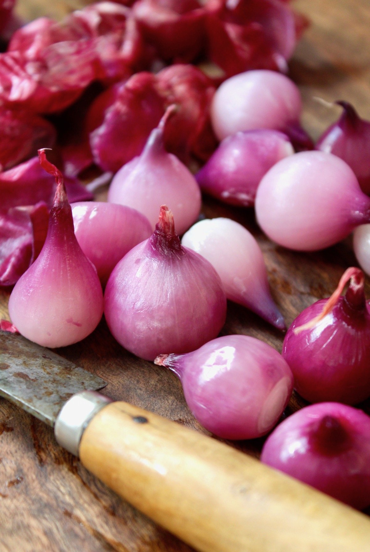 peeled red pearl onions on cutting board with knife