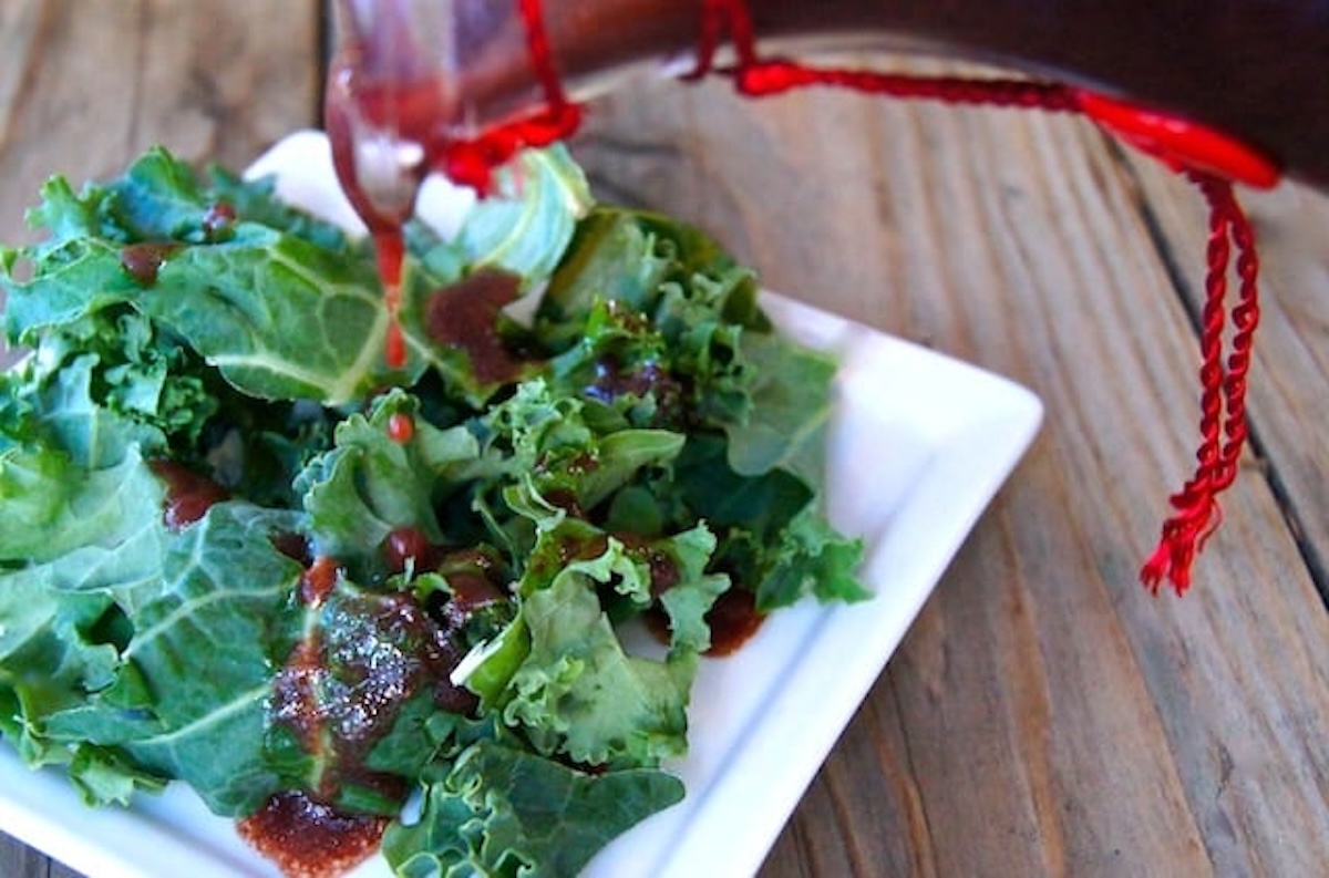 Balsamic-Cranberry-Dressing-Recipe Greens with cranberry dressing being drizzled over them.