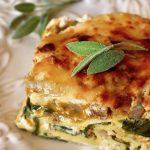 One slice of butternut squash and spinach lasagna on a white plate with fresh sage leaves.