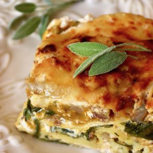 One slice of butternut squash and spinach lasagna on a white plate with fresh sage leaves.