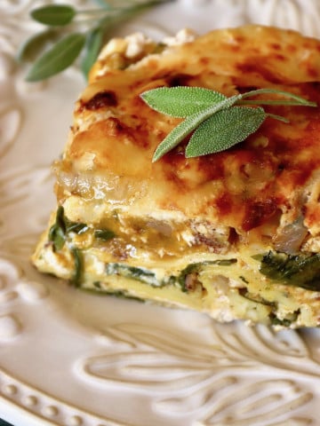 One large slice of butternut squash lasagna with chicken on a white plate with fresh sage leaves.