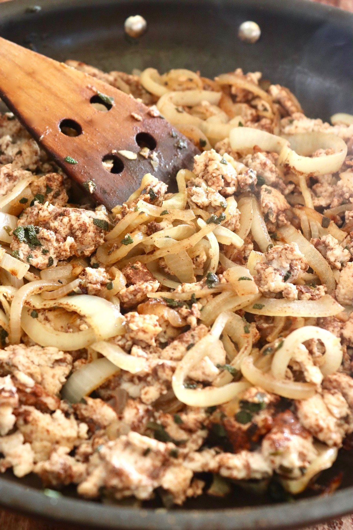 Saute pan with wooden spatula, ground cooked chicken, sliced onion and sage.