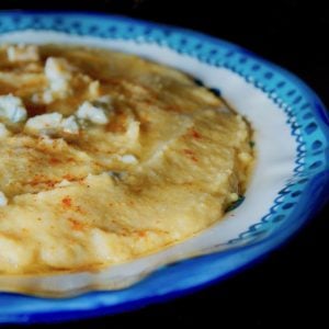 Creamy polenta in a blue-rimmed bowl with crumbled blue cheese on top.