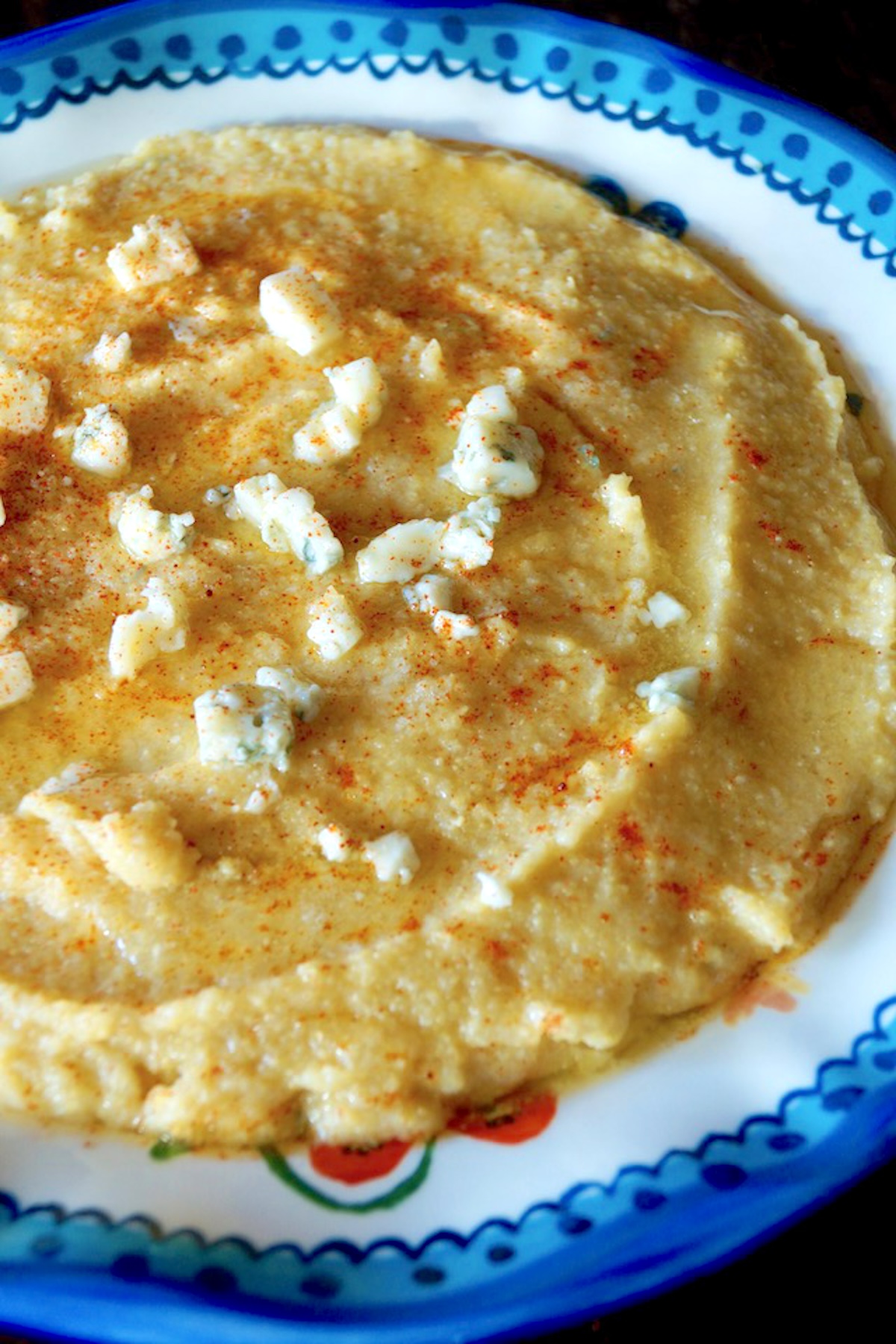 Creamy-Gorgonzola-Polenta-Recipe Bright blue-rimmed bowl with creamy polenta with gorgonzola sprinkled on top.