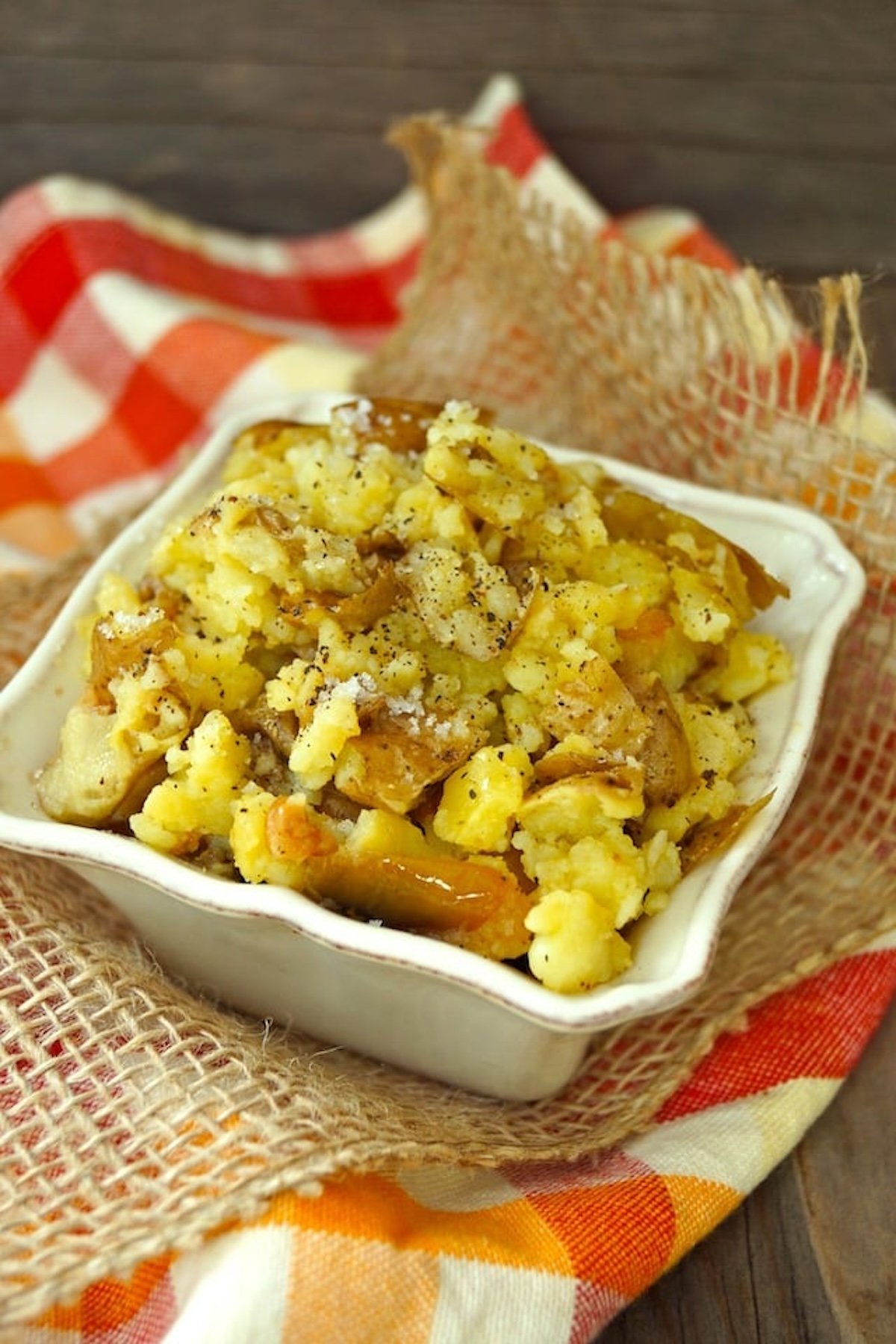 Rustic Garlic Confit Mashed Potatoes in a square white bowl on a red and white checkered cloth.