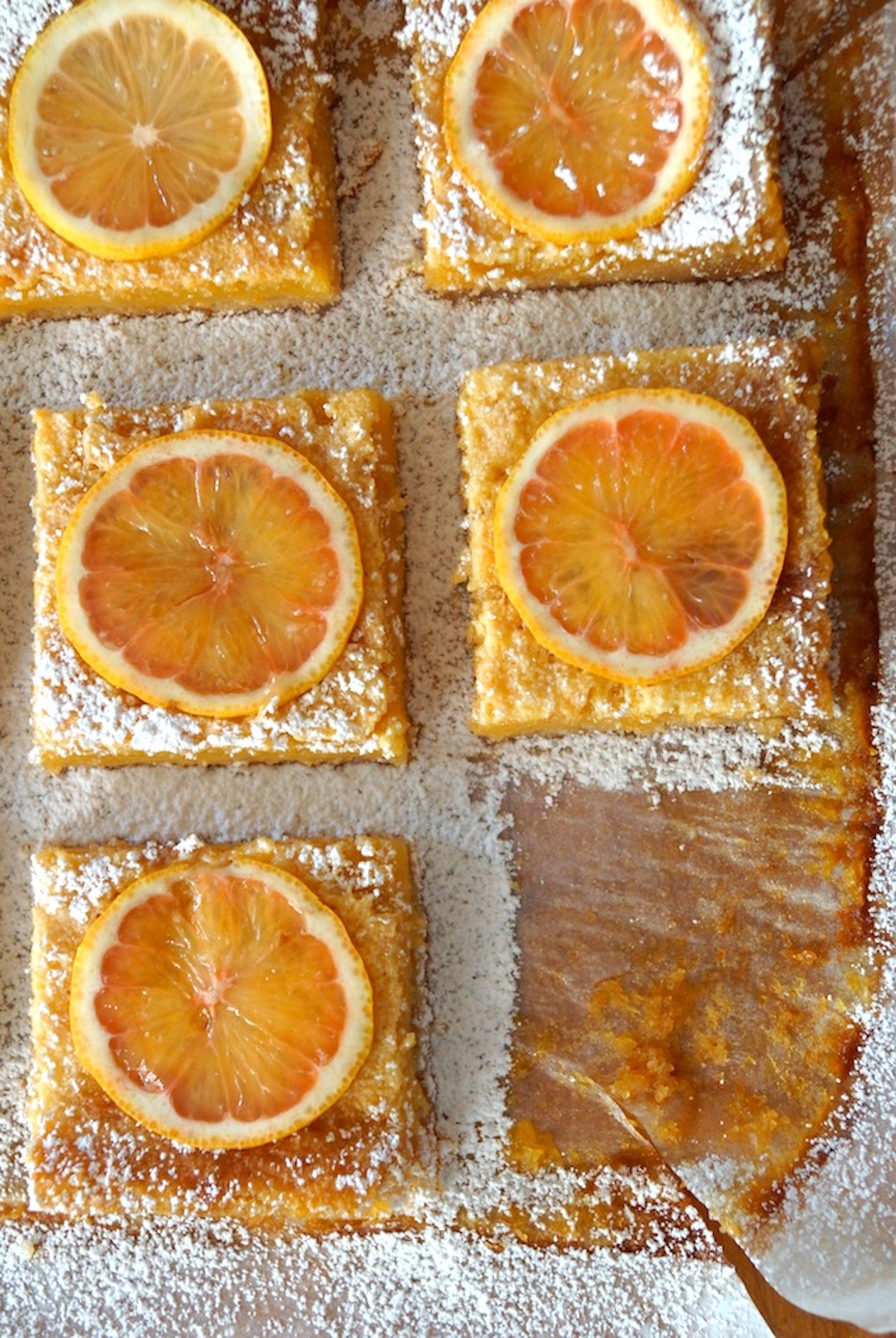 8 evenly spaced lemon bars that are square, on parchment paper, with evidence of a 9th one missing.