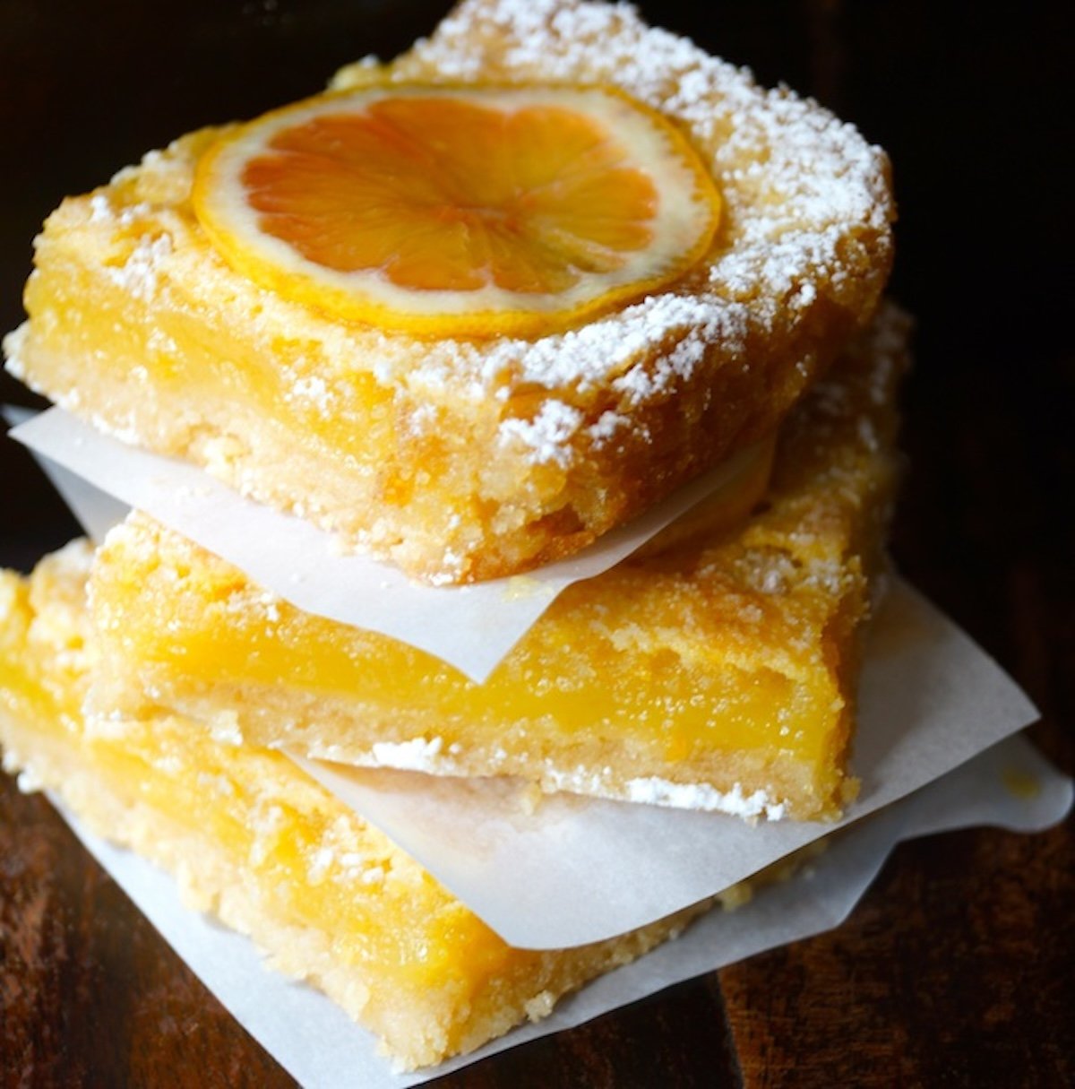 Stack of 3 lemon bars with parchment between them.