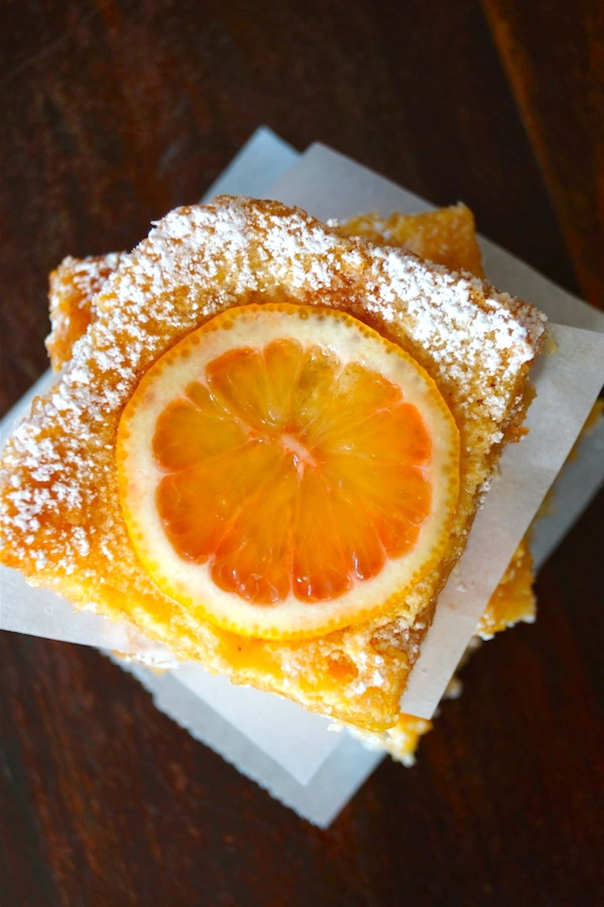 Top view of stack of Pink lemon bars with pieces of parchment between them.