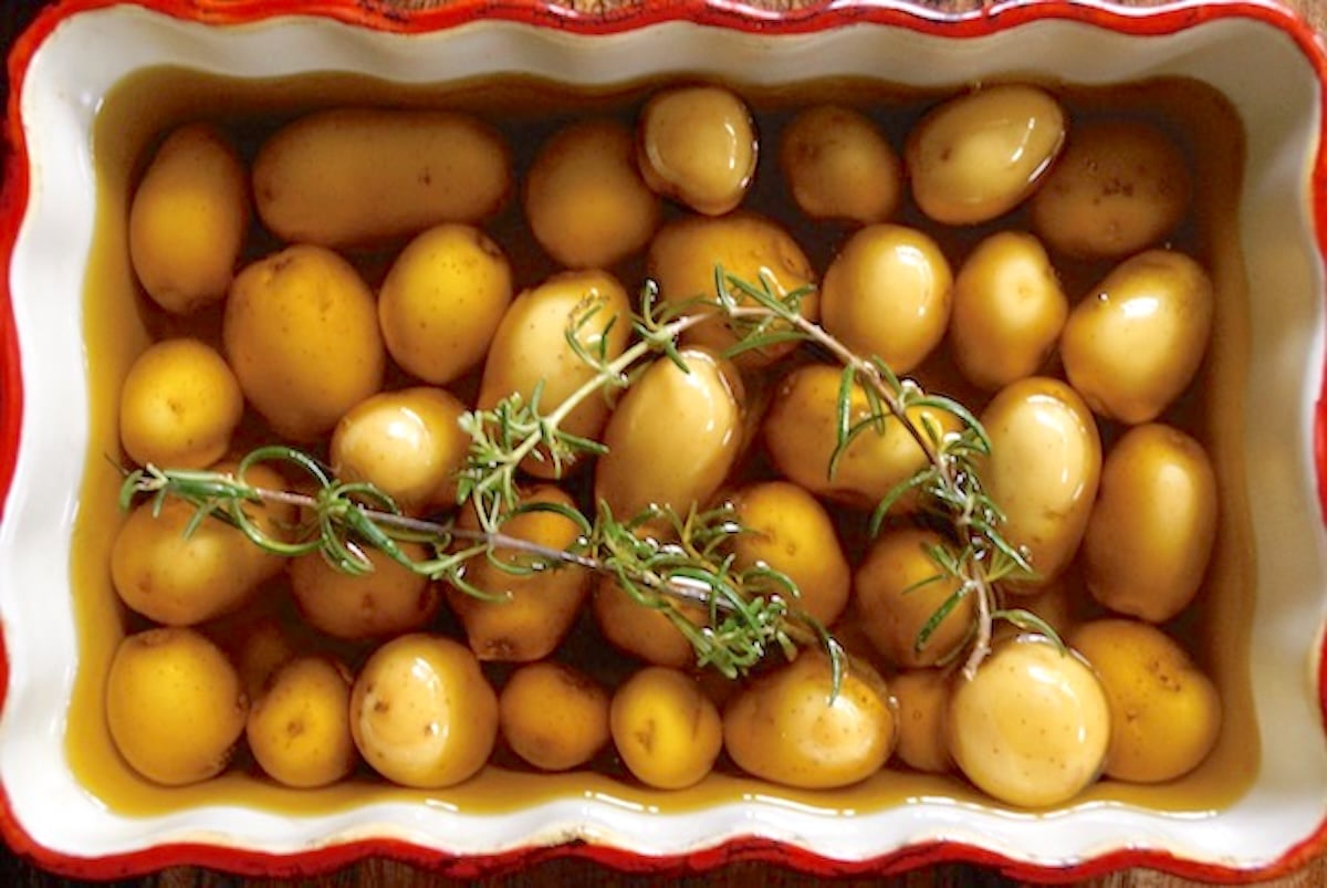 Pee Wee potatoes covered with olive oil and rosemary sprigs in a red-rimmed baking dish.