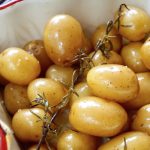 Confit potatoes with rosemary sprig in a red-rimmed baking dish.
