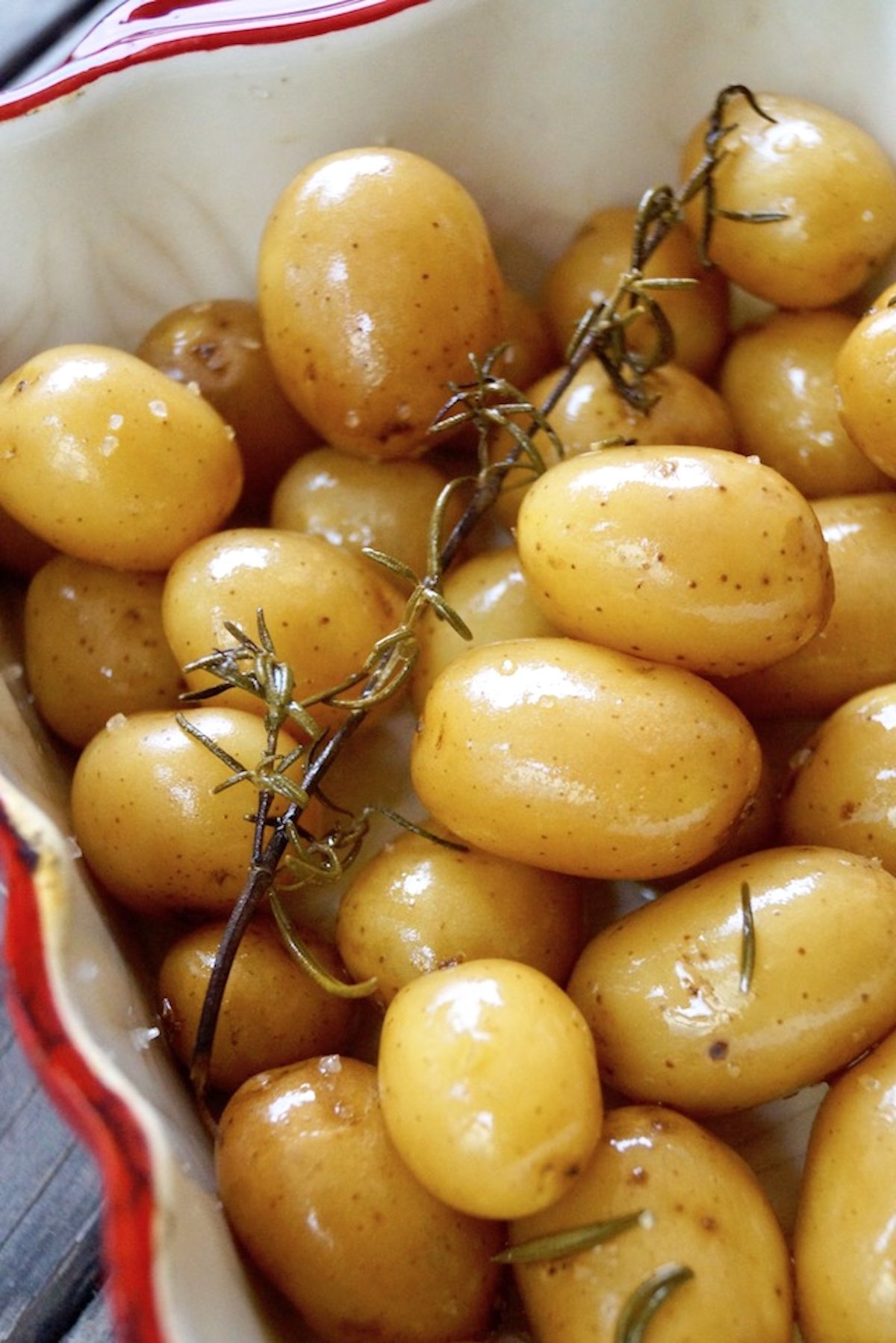 Confit potatoes with rosemary sprig in a red-rimmed baking dish.
