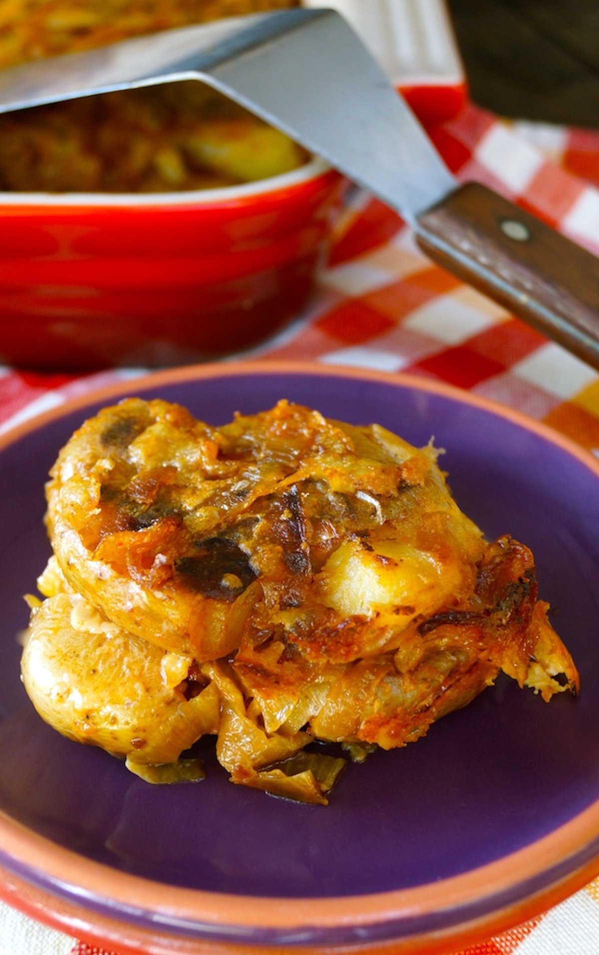 Slice of smashed potato casserole with caramelized on a purple plate.