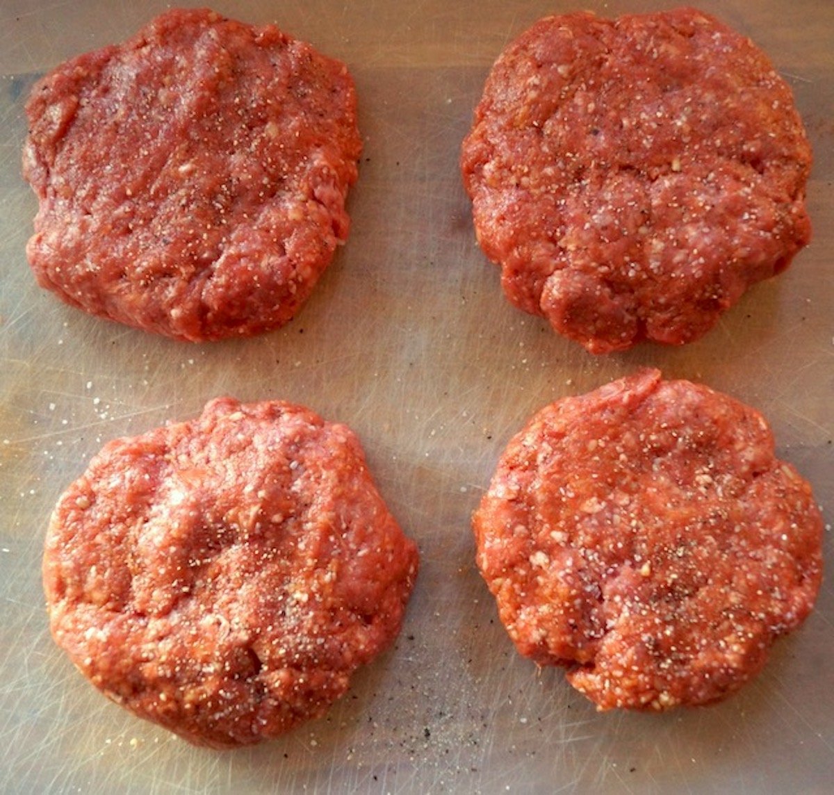 Four shaped raw beef burgers on clear cutting sheet.