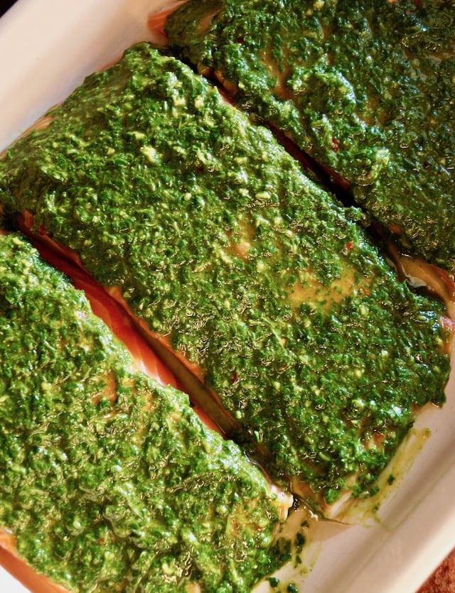 Three raw fillets of salmon with chimichurri spread over them