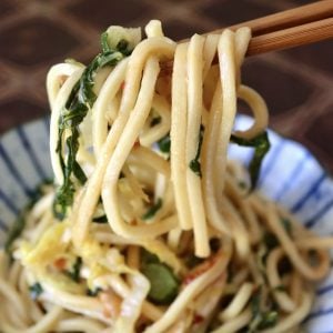 Serving of Chinese Longevity Noodles with Gai Lan on ceramic blue and white plate with a bite held up in chopsticks.