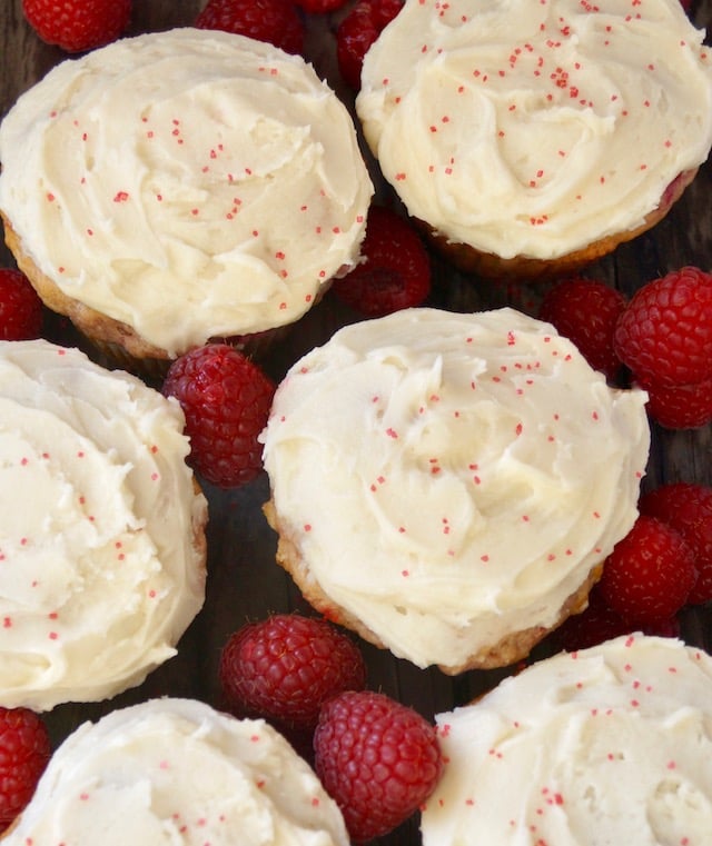 several butercream-frosted raspberry cupcakes with raspberries between them