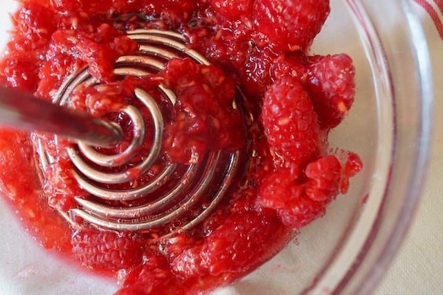 fresh raspberries being mashed in glass bowl