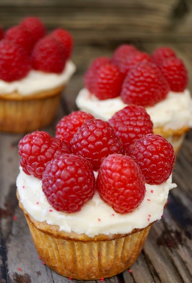 three fresh raspberry cupcakes with raspberries on top