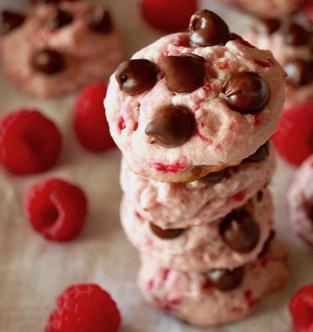 Pila di 4 Valentines' Day Raspberry Chocolate Cookies circondati da lamponi rossi freschi.