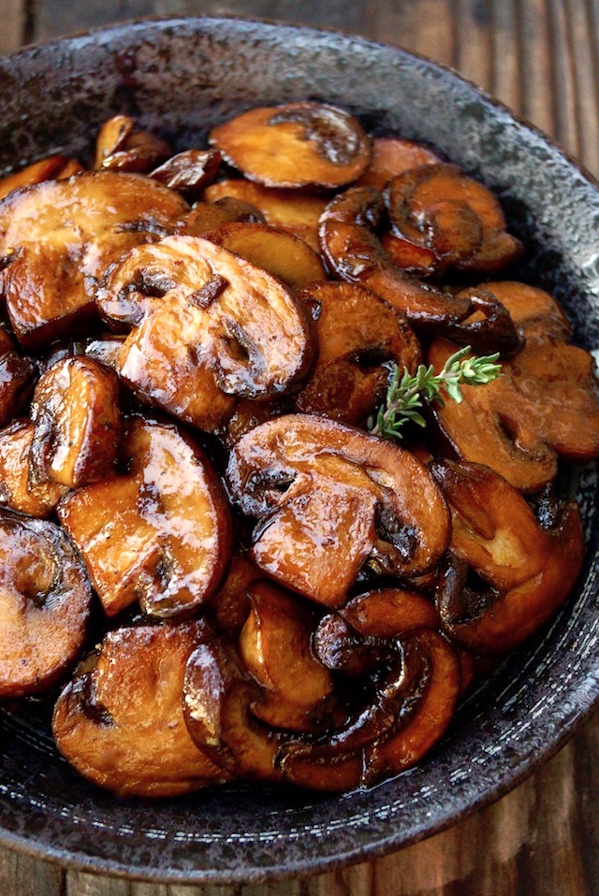 Super golden caramelized sliced button mushrooms in a black ceramic bowl.