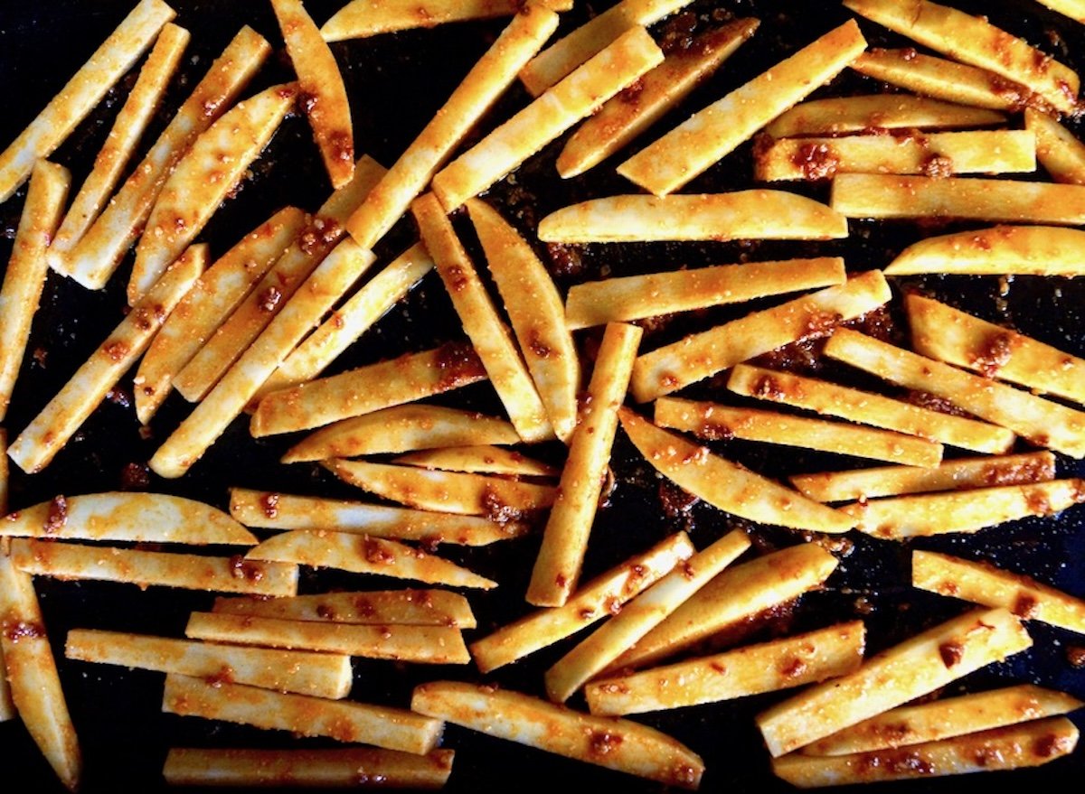 Raw chipotle parmesan fries spread out on a black baking sheet.
