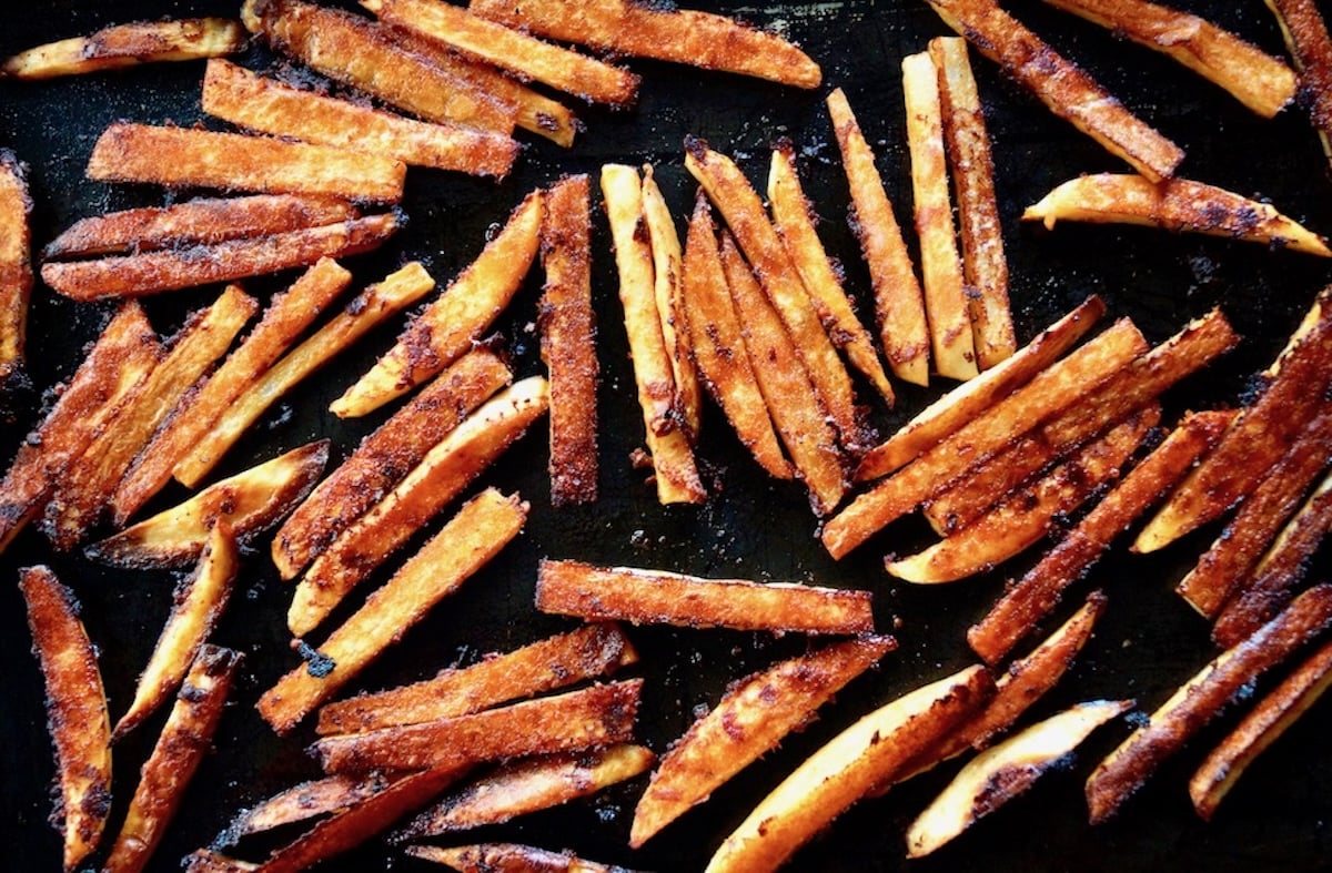 Roasted chipotle parmesan fries spread out on a black baking sheet.