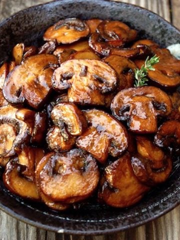 browned mushrooms in black bowl on wood surface