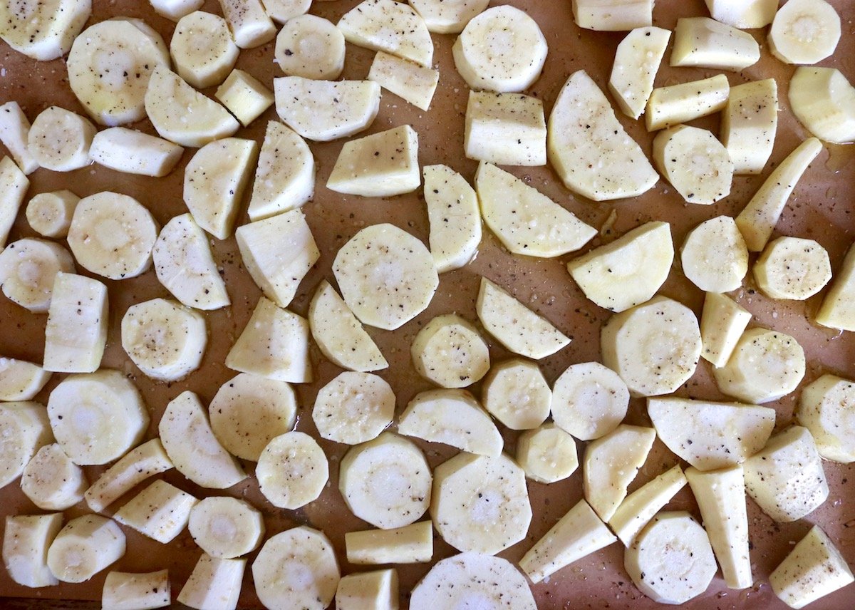 Raw and chopped parsnips on a baking sheet.