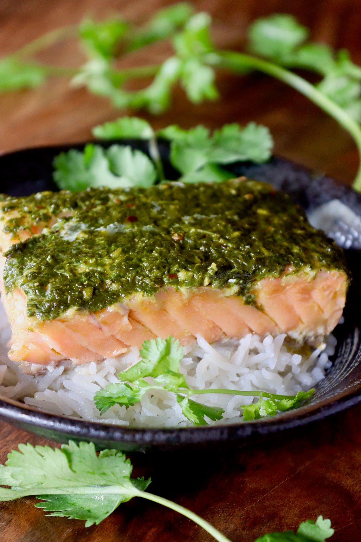 Fillet of Cilantro Chimichurri Salmon on rice in black bowl over rice.