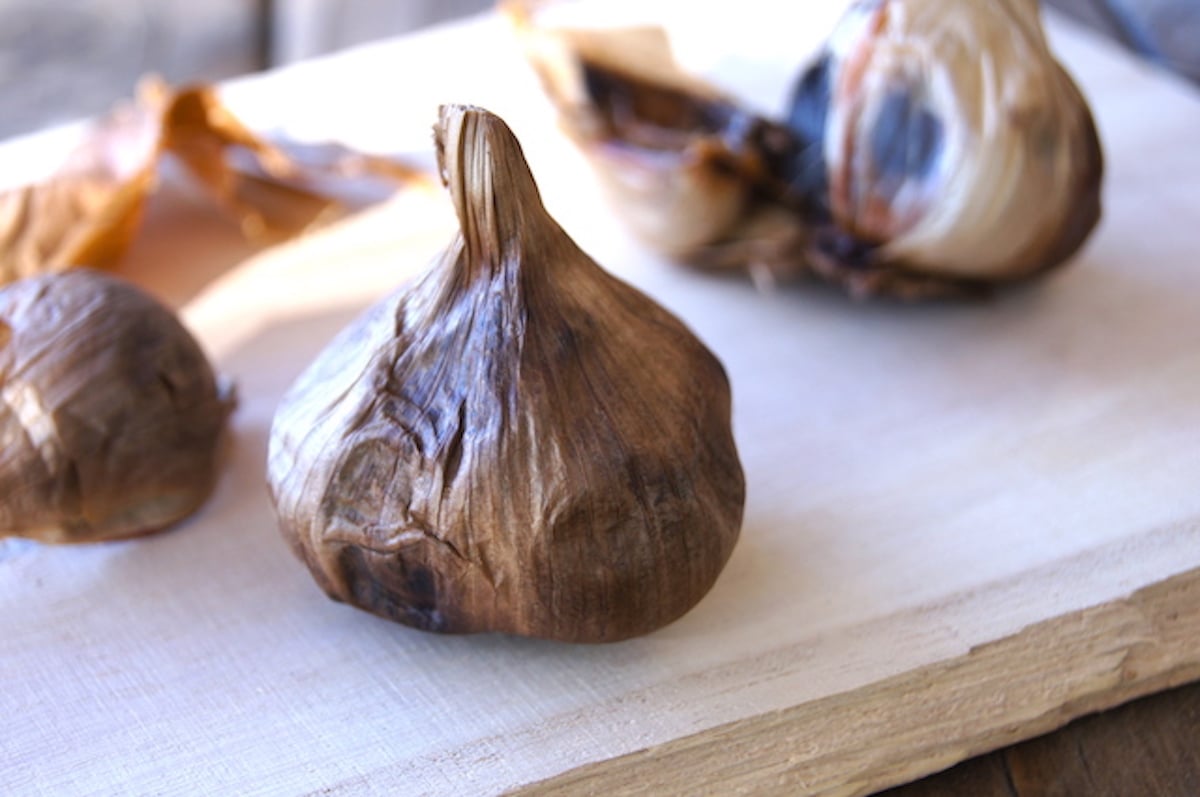 Large head of black garlic on light wood board.