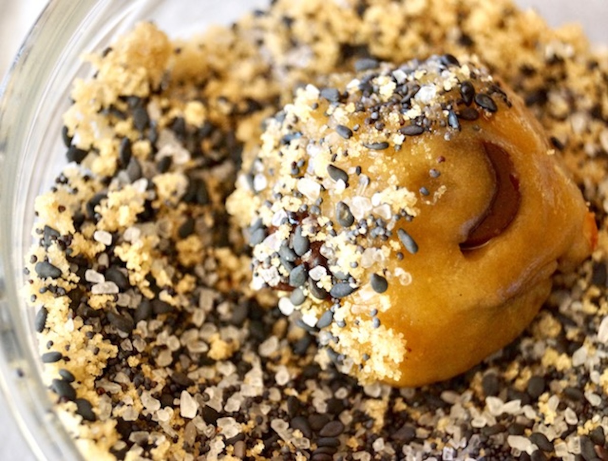 Chocolate chip cookie dough ball sitting in mix of poppy and sesame seeds.
