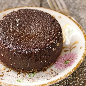 Flourless Chocolate Kahlua Espresso Decadence Cake on a pretty, gold-rimmed plated with pink flowers, dusted with powdered sugar.