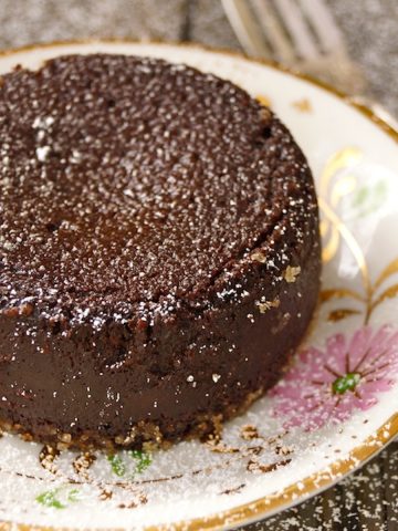 Flourless Chocolate Kahlua Espresso Decadence Cake on a pretty, gold-rimmed plated with pink flowers, dusted with powdered sugar.