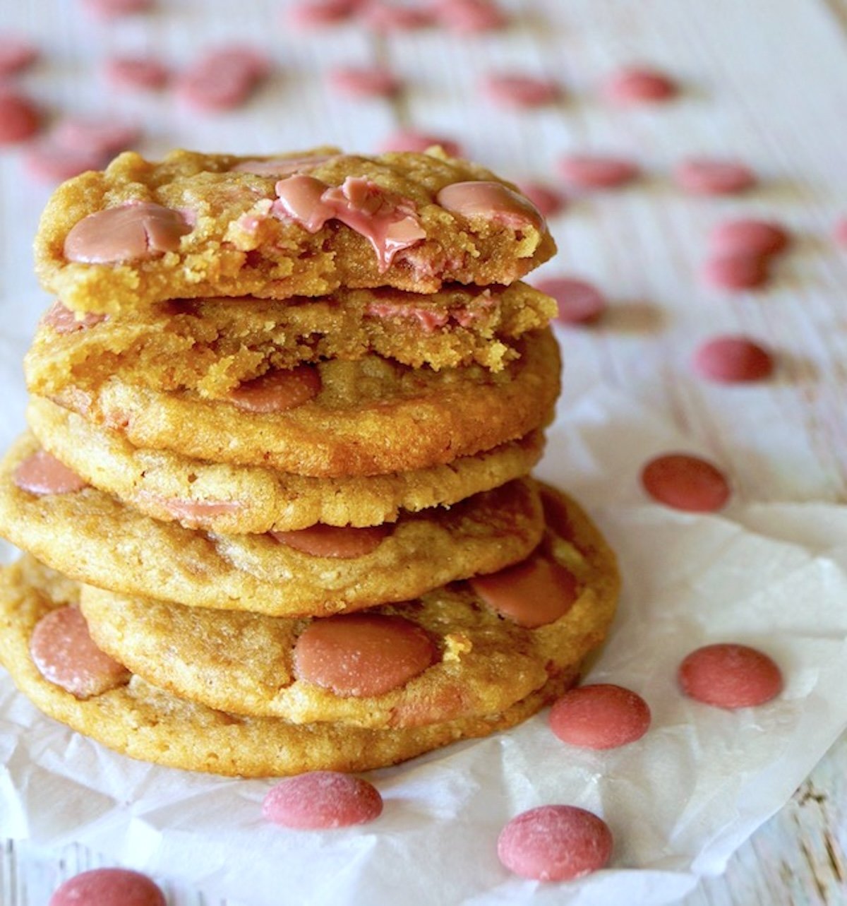 Stack of chocolate chip cookies with pink (ruby) chocolate chips, with the top cookie broken in half, surrounded by more chips.