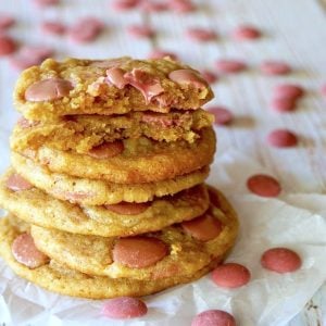 Stack of chocolate chip cookies with pink (ruby) chocolate chips, with the top cookie broken in half, surrounded by more chips.