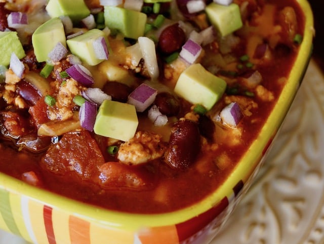 Close up of Striped colorful bowl with Vegetarian Tofu Chili with avocado on top