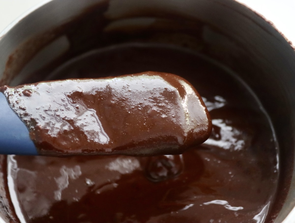 Flourless Chocolate-Cake-with-KahlĂșa-and-Espresso Chocolate sauce in saucepan with some being held up on a spatula.