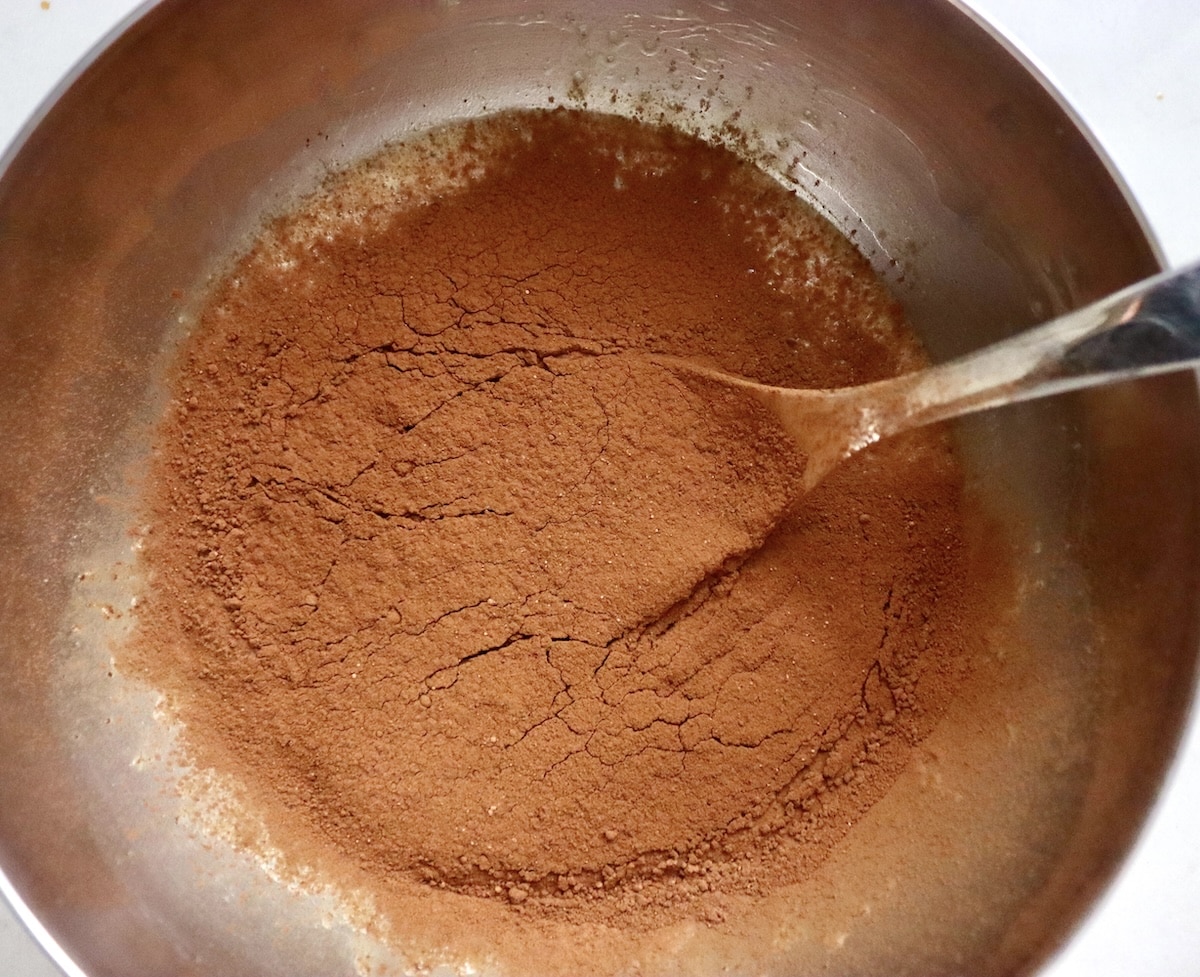 Flourless Chocolate-Cake-with-KahlĂșa-and-Espresso Batter for chocolate espresso flourless cakes in a stainless steel bowl with cocoa powder on top and a spoon.