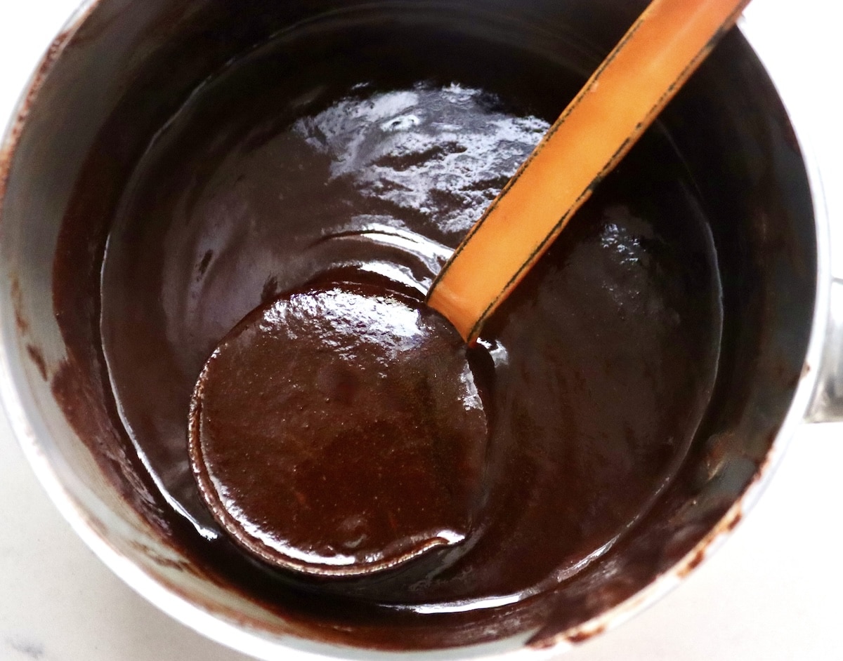 Flourless Chocolate-Cake-with-KahlĂșa-and-Espresso Chocolate espresso sauce in small saucepan with orange, metal ladle.