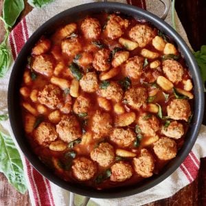 Turkey meatballs and gnocchi in a large skillet with basil leaves.