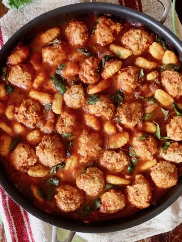 Turkey meatballs and gnocchi in a large skillet with basil leaves.