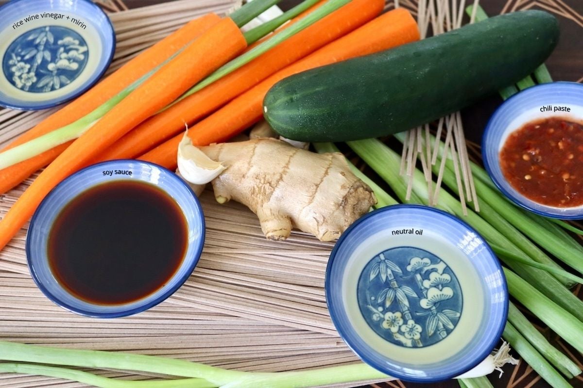 Ingredients for soba noodle salad including carrots, ginger, cucumber, soba noodles and garlic, plus soy sauce.