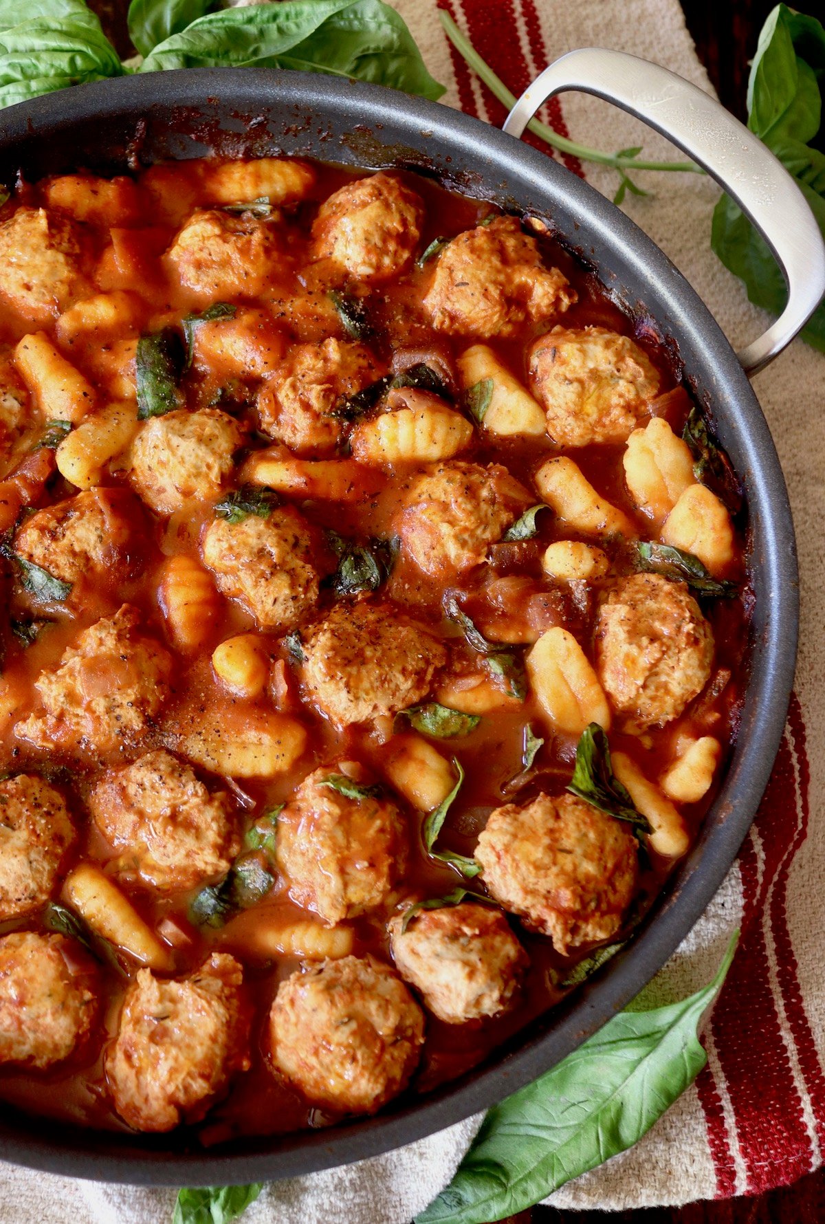 Close up of turkey meatballs and gnocchi in a large skillet with basil leaves.