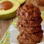 Small stack of chocolate cookies made with avocado and a halved avocado behind it.