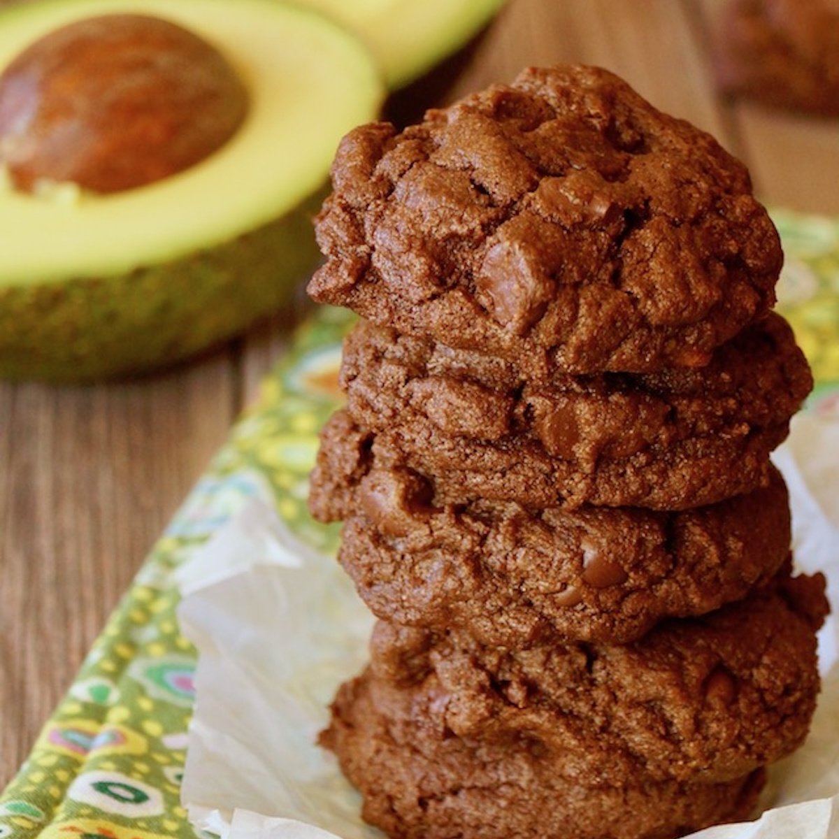 Small stack of chocolate cookies made with avocado and a halved avocado behind it.