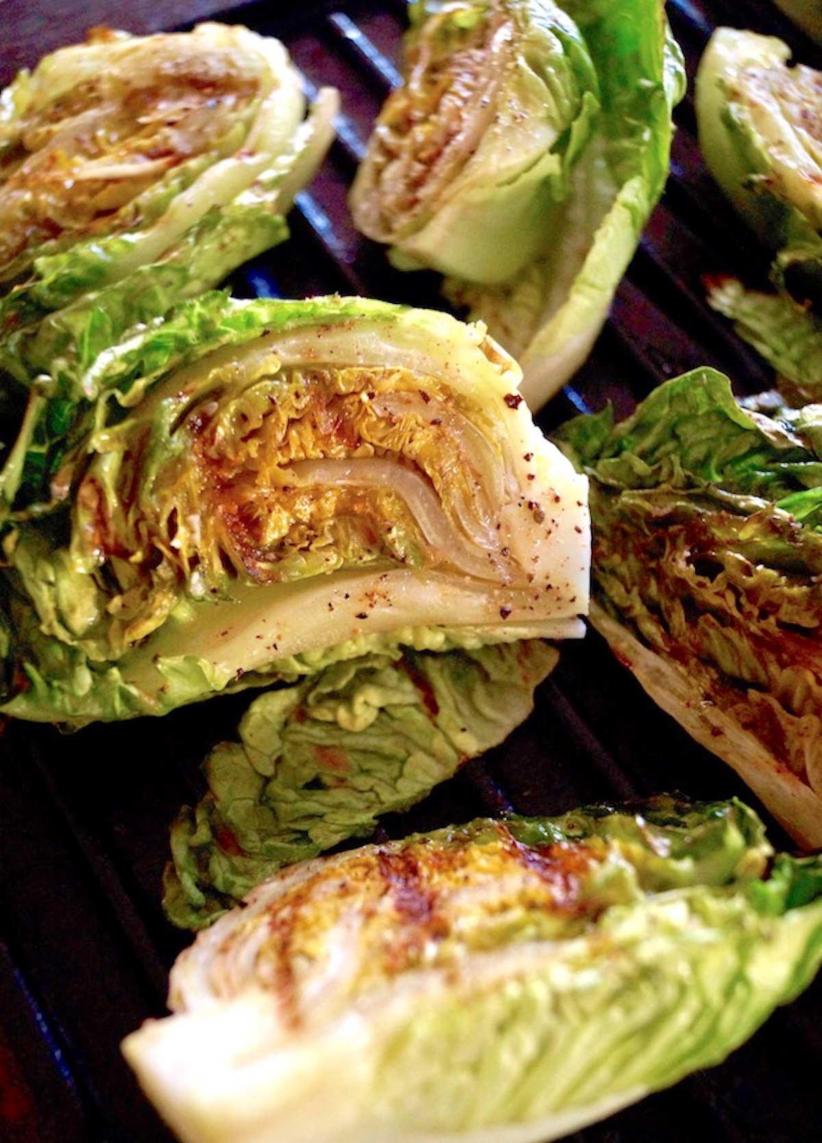 Grilled-Little-Gem-Lettuce-Salad A few heads of little gem lettuce cut in half and grilled on a black surface.