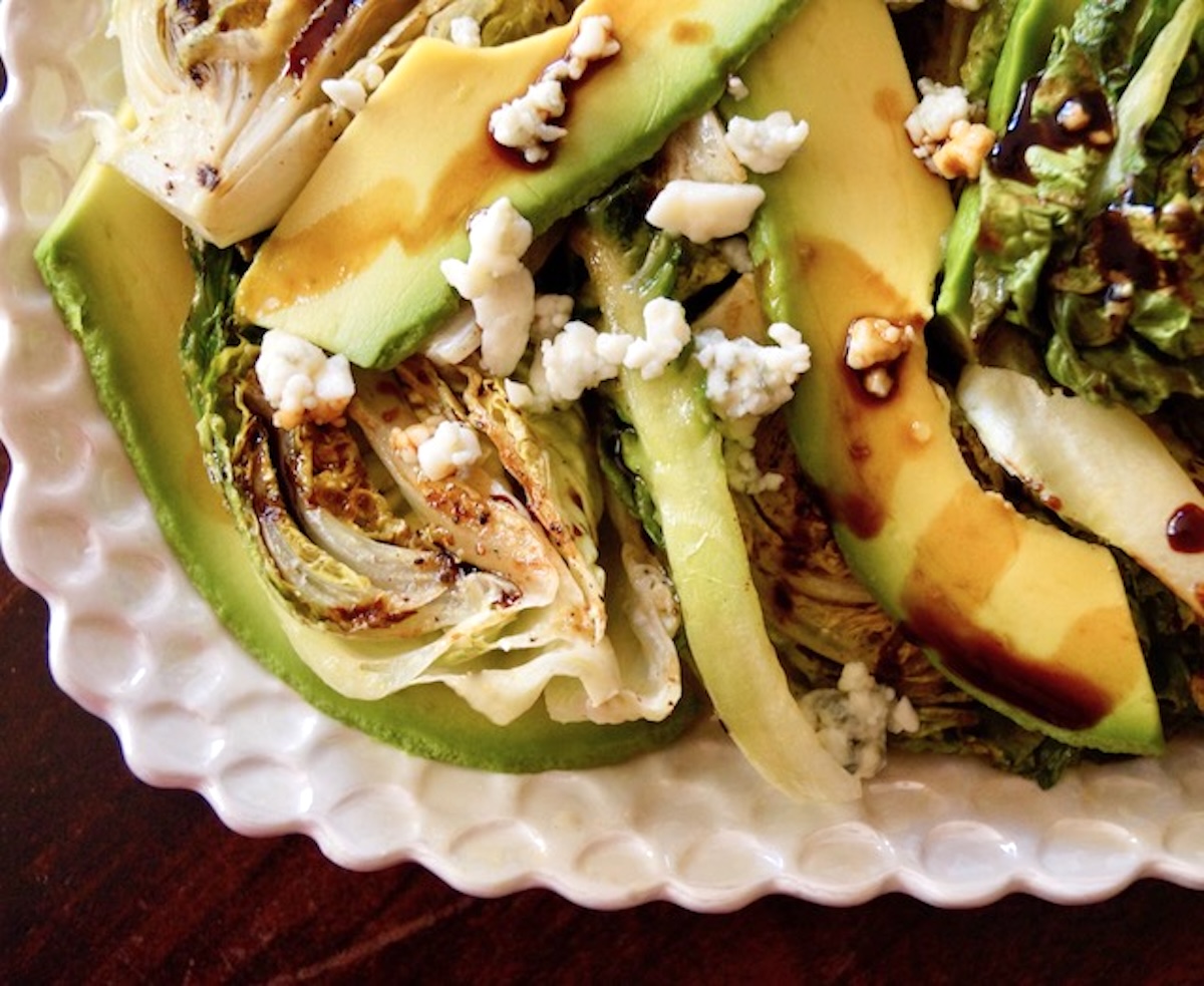 Grilled-Little-Gem-Lettuce-Salad Close up of Little Gem Salad on a white plate with avocado and bits of blue cheese.
