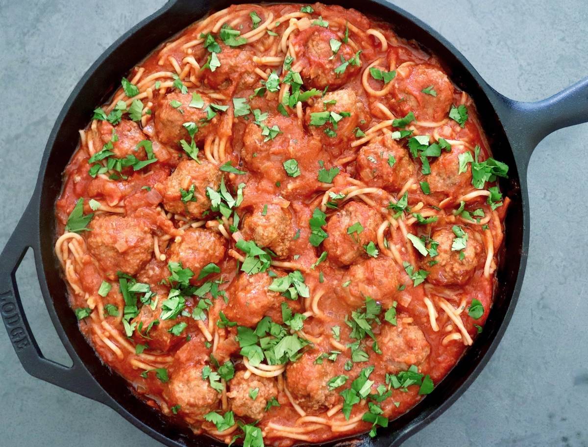 Cast iron skillet full with spaghetti and meatballs with Sriracha sauce.