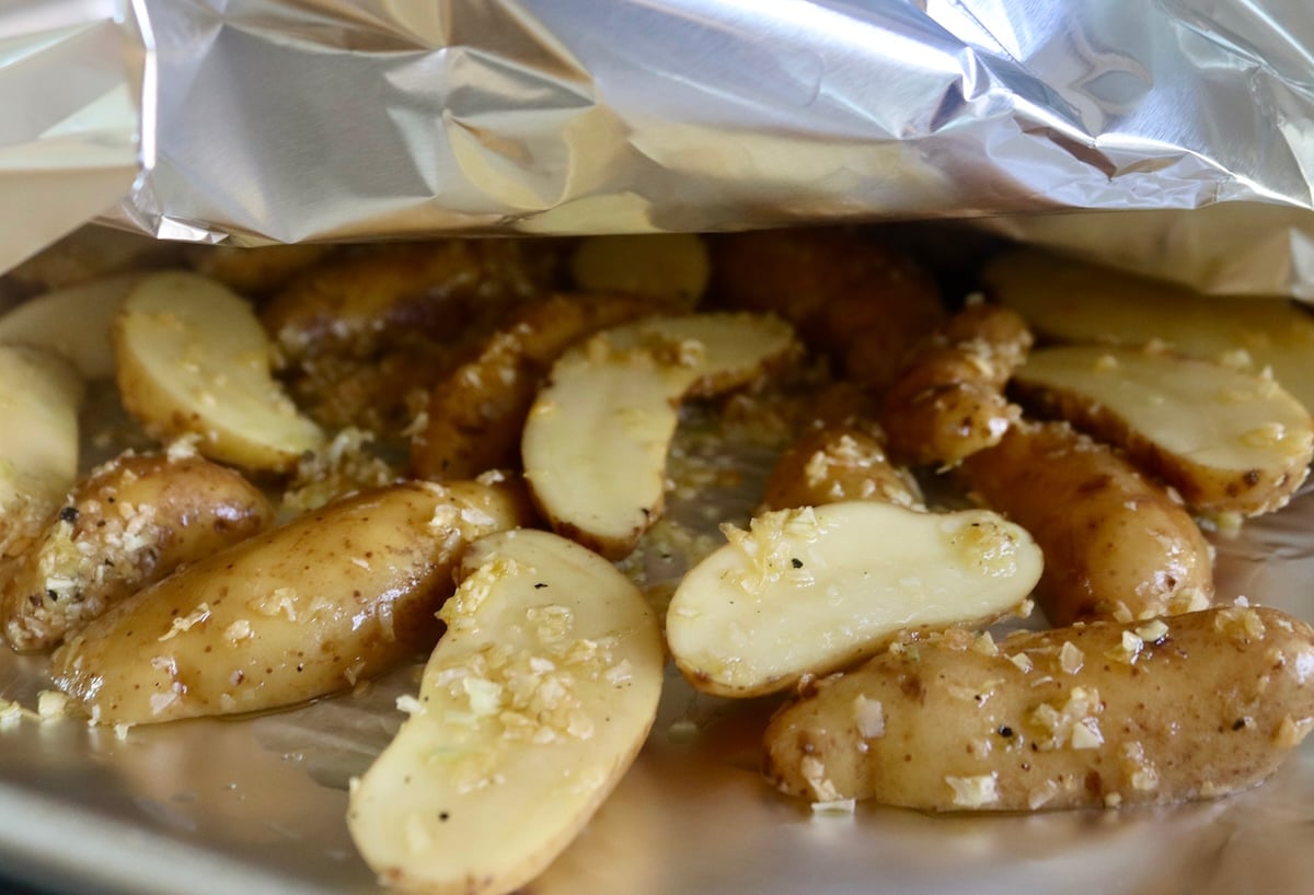 Sheet pan with two pieced of foil, with sliced potatoes between them.