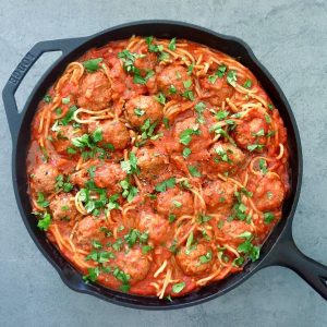 Cast iron skillet full with spaghetti and meatballs with sriracha sauce.